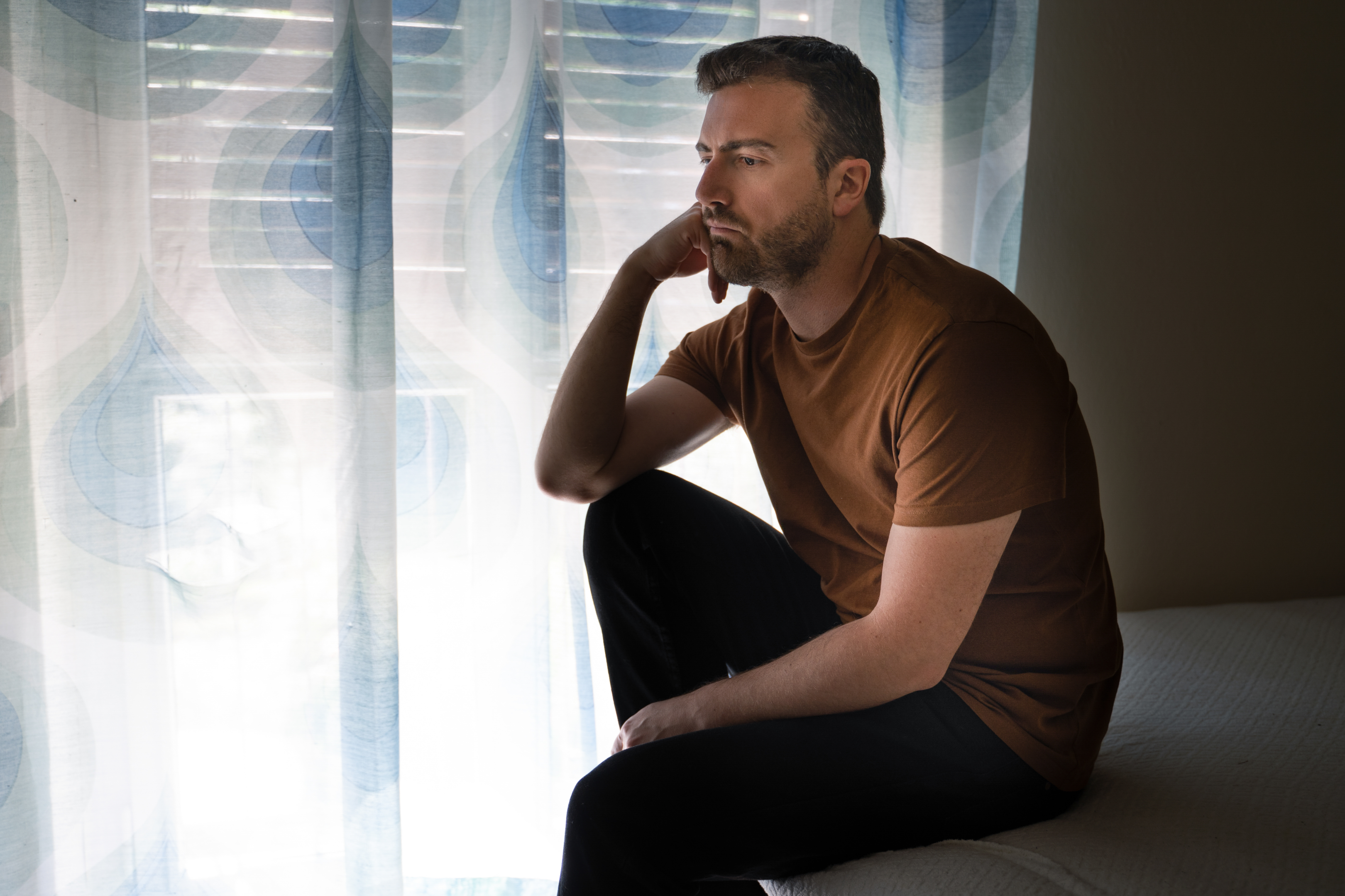 man sitting on a couch with hand on his chin in a deep state of thought