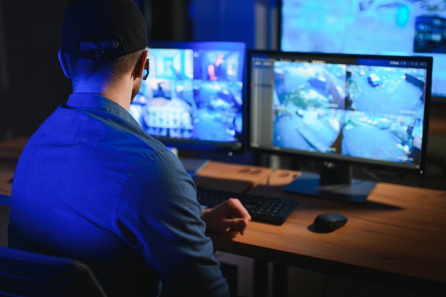 A security officer is focused on multiple high-definition screens showing a cloud surveillance system monitoring outdoor and indoor spaces. The modern security systems ensure workplace security and controlled secure office entry.