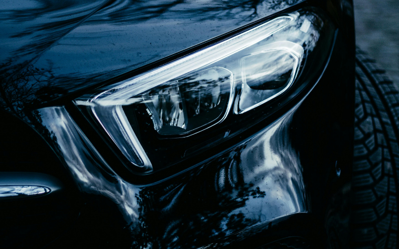 Close-up of a black car headlight and paint job showing reflections after car washing