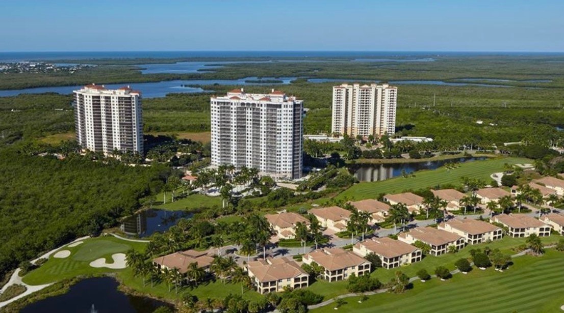An aerial view of Hammock Bay Golf and Country Club showcases luxury tower residences surrounded by championship golf courses and lush natural areas. The image highlights the exclusive lifestyle of this prestigious community, featuring resort-style amenities such as a pool and beautifully landscaped grounds.