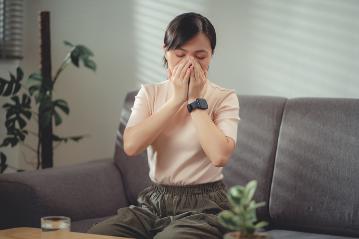 An image of a woman with a seasonal sore throat sneezing into her cupped hands. 