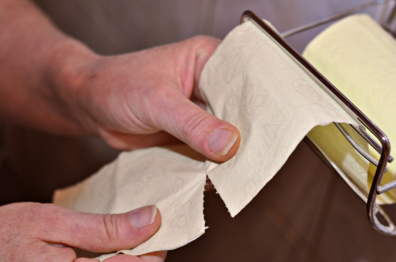 An image of a man's hand tearing a piece of toilet paper of a roll in the bathroom.