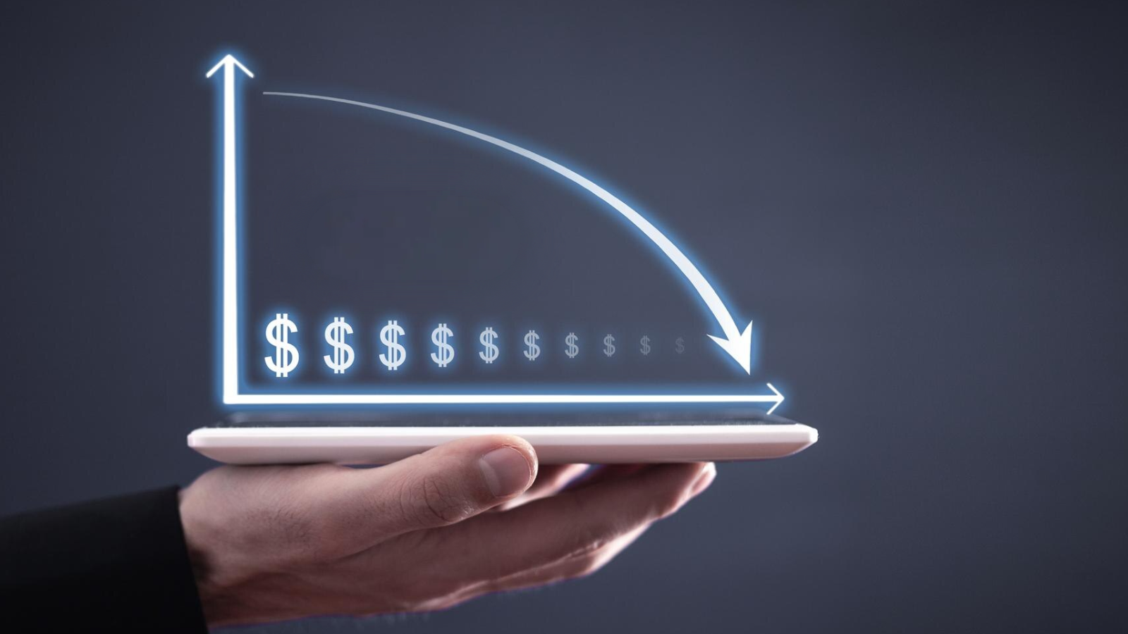 Person holding a tablet displaying a glowing downward graph with dollar signs, representing cost reduction achieved by switching from traditional PBX to cloud-based business VoIP solutions.