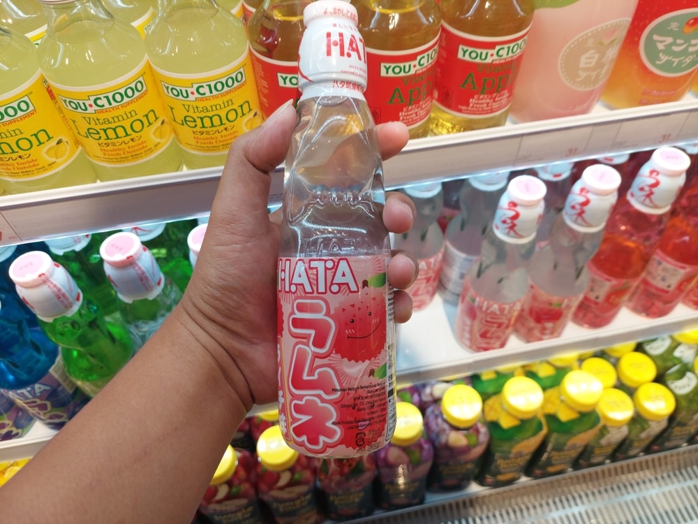 Magelang, Indonesia - August 18, 2024  Hands holding and selecting Hata Kosen's Ramune Blueberry Drink. Colorful bottles of Hata brand Japanese soda Ramune are neatly arranged in the KKV store.