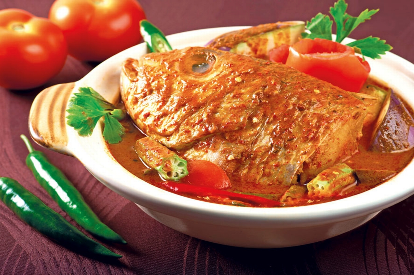 A vibrant bowl of Fish Head Curry with fish, assorted vegetables, and a savory tomato sauce.