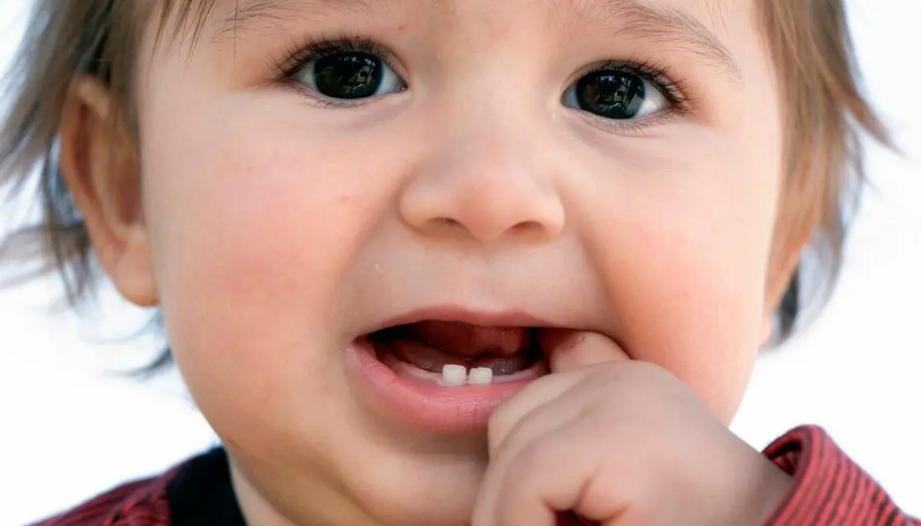 Baby med de første melketennene tygger på fingeren mens nye tenner vokser frem i tannkjøttet.