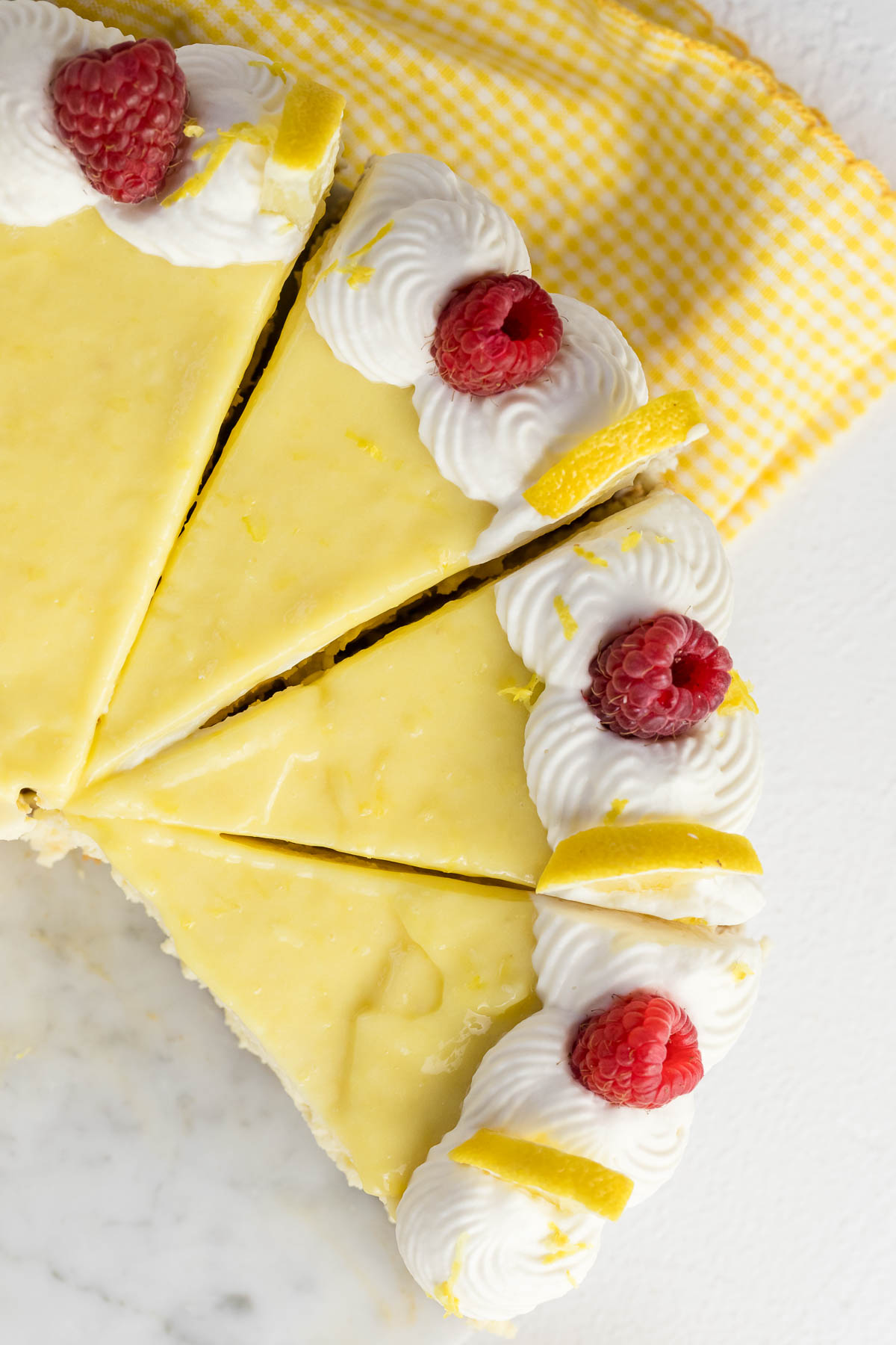 lemon cheesecake cut into slices topped with lemon curd, whipped cream and raspberries
