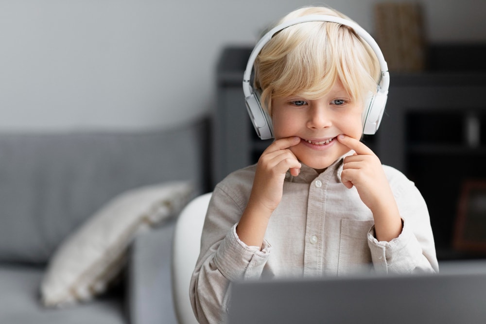 blonde boy with earphones on smiling in front of laptop