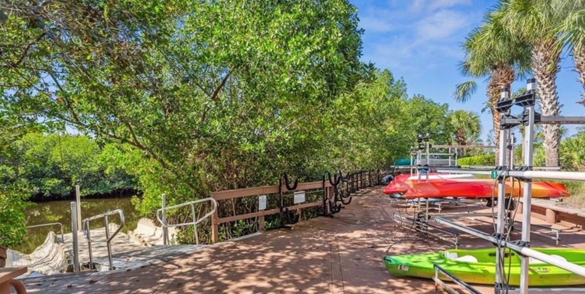 The image depicts a serene natural wetland area in Bonita Springs, featuring cypress trees and native vegetation that beautifully reflect in the still water, showcasing the natural beauty of the region. This tranquil scene highlights the pristine wetlands that are part of the Pelican Landing community, known for its exceptional living experience and rich natural landscapes.