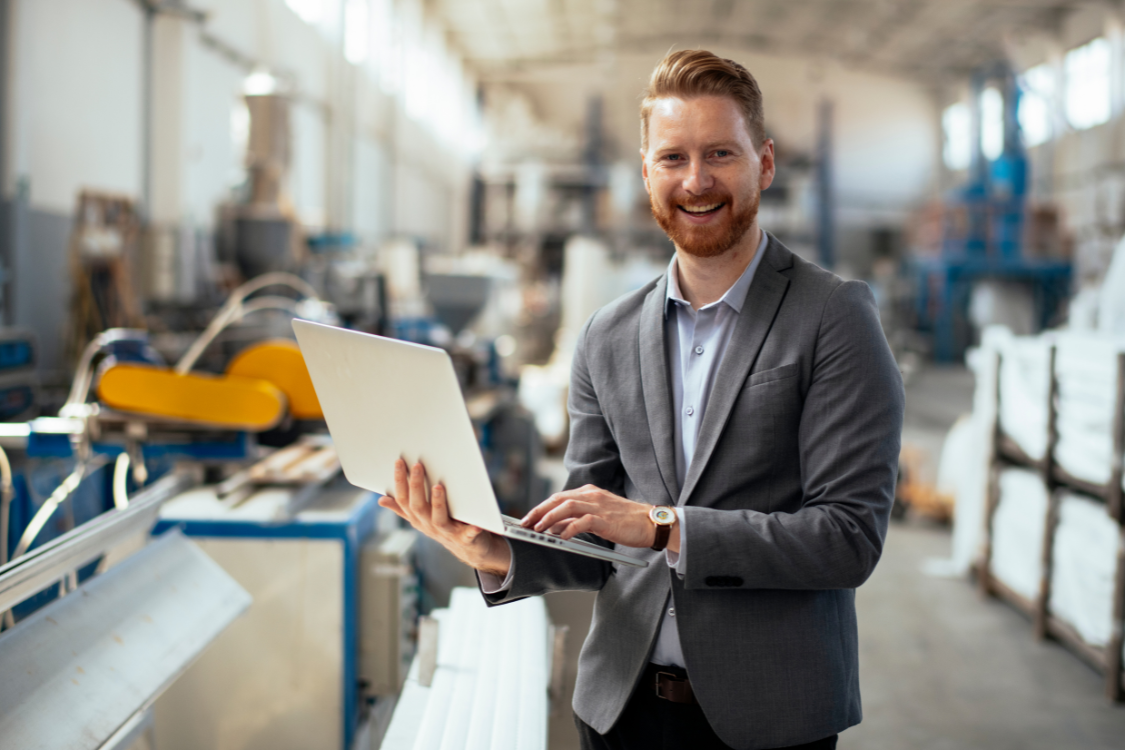 Smiling supplement manufacturer reviewing production data on laptop in a facility