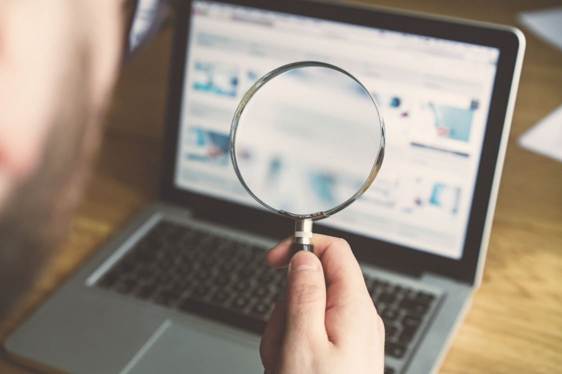 Person using magnifying glass to examine broker listings on a laptop during a Google search