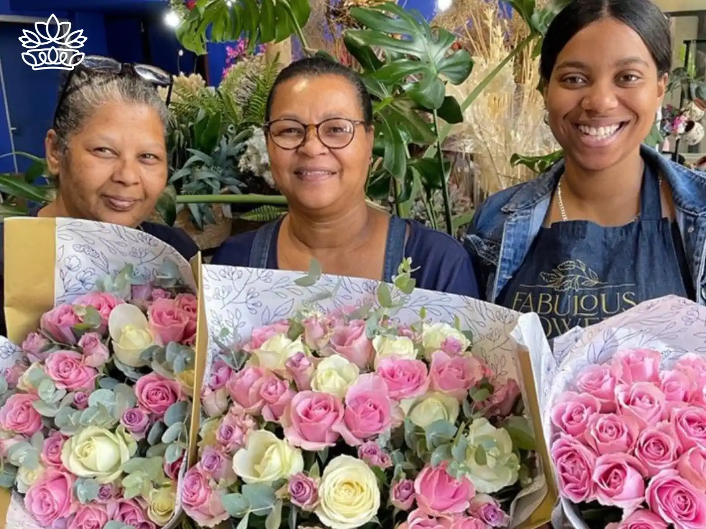 Three joyful florists holding lush bouquets of pink and cream roses surrounded by eucalyptus leaves, a bespoke creation from Fabulous Flowers and Gifts.