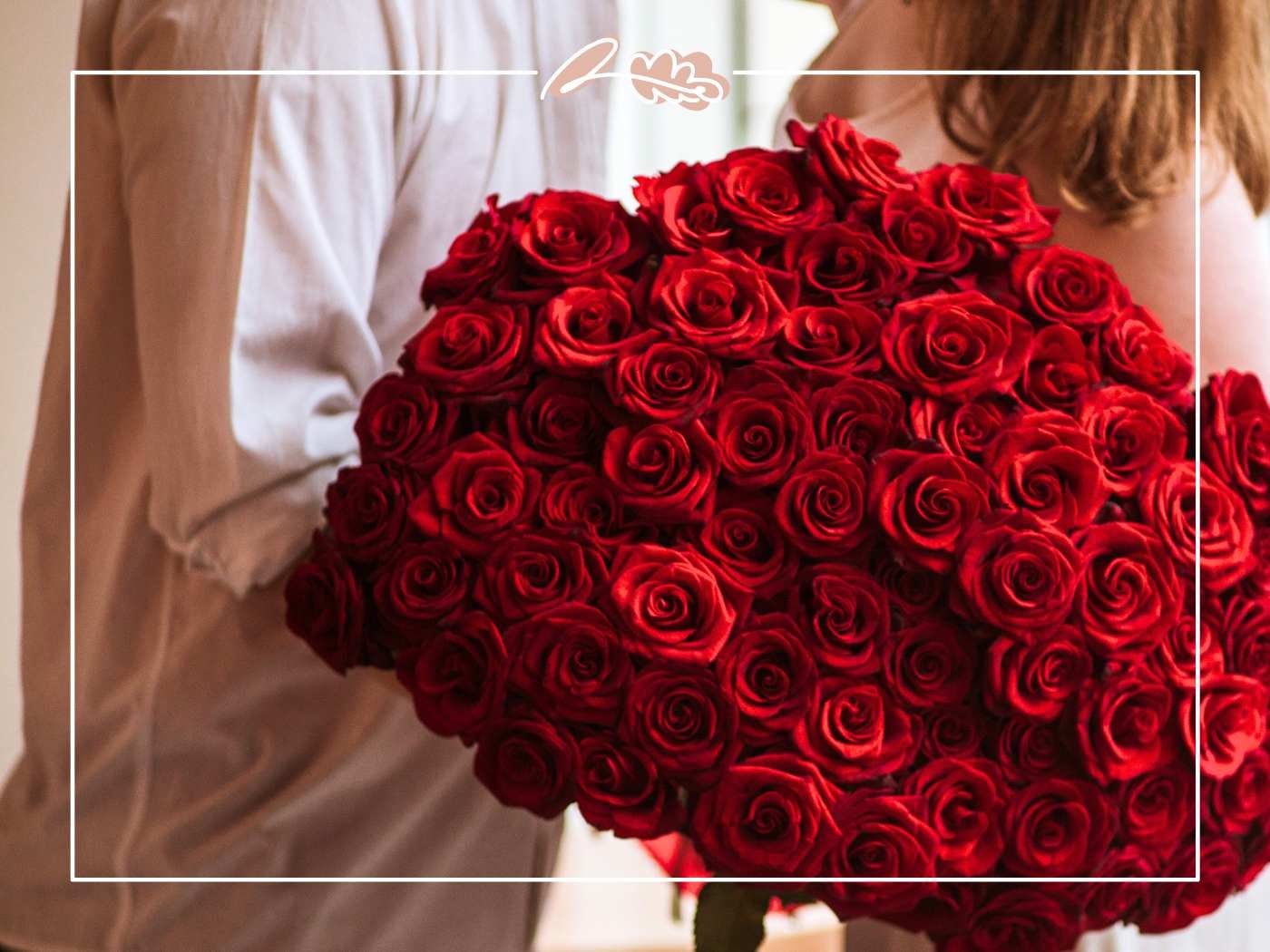 Couple holding a large bouquet of red roses in warm light, romantic close-up, Fabulous Flowers border.