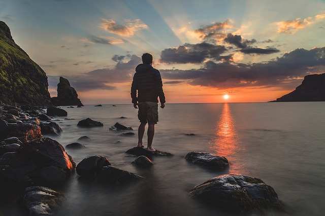 Pexels from Pixabay. Man standing on rocks in ocean watching sunset. 