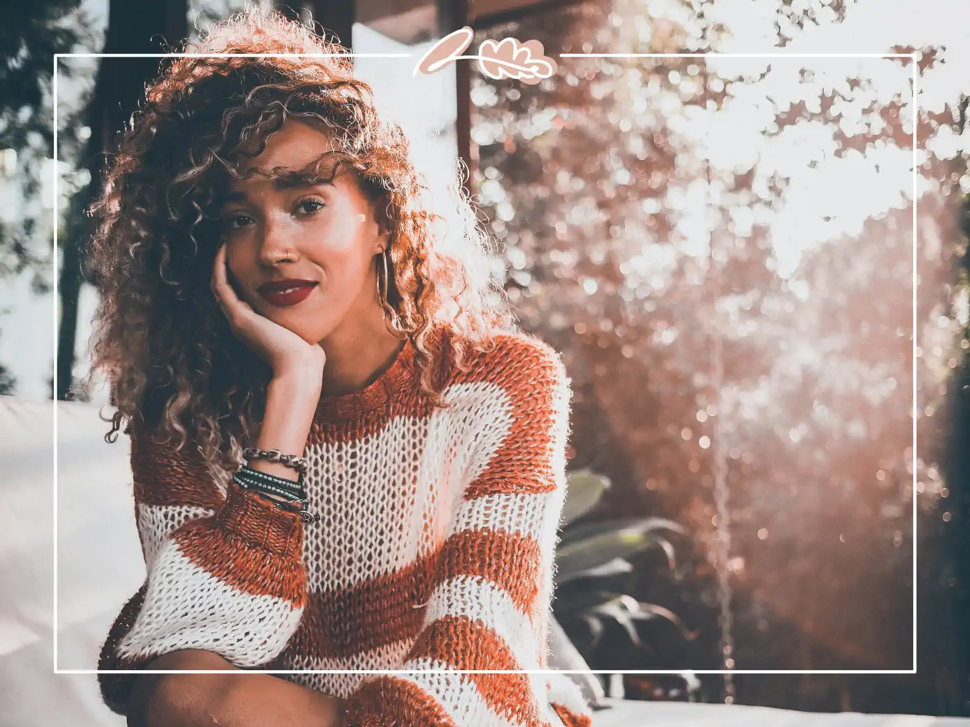 A woman with curly hair in a cosy striped sweater, sitting thoughtfully by the window. Fabulous Flowers and Gifts.