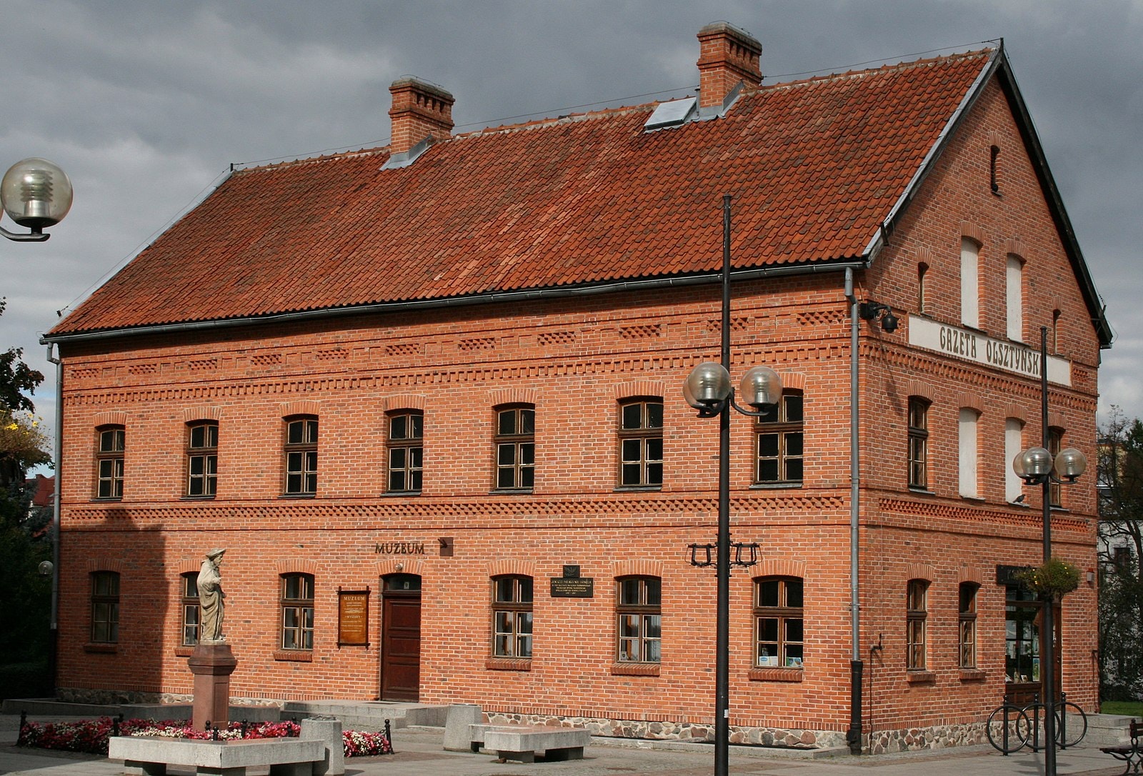 Muzeum z czerwonej cegły, przed którego budynkiem znajduje się rzeźba. Źródło: https://commons.wikimedia.org/wiki/File:KP,_dom_Gazety_Olszty%C5%84skiej.JPG