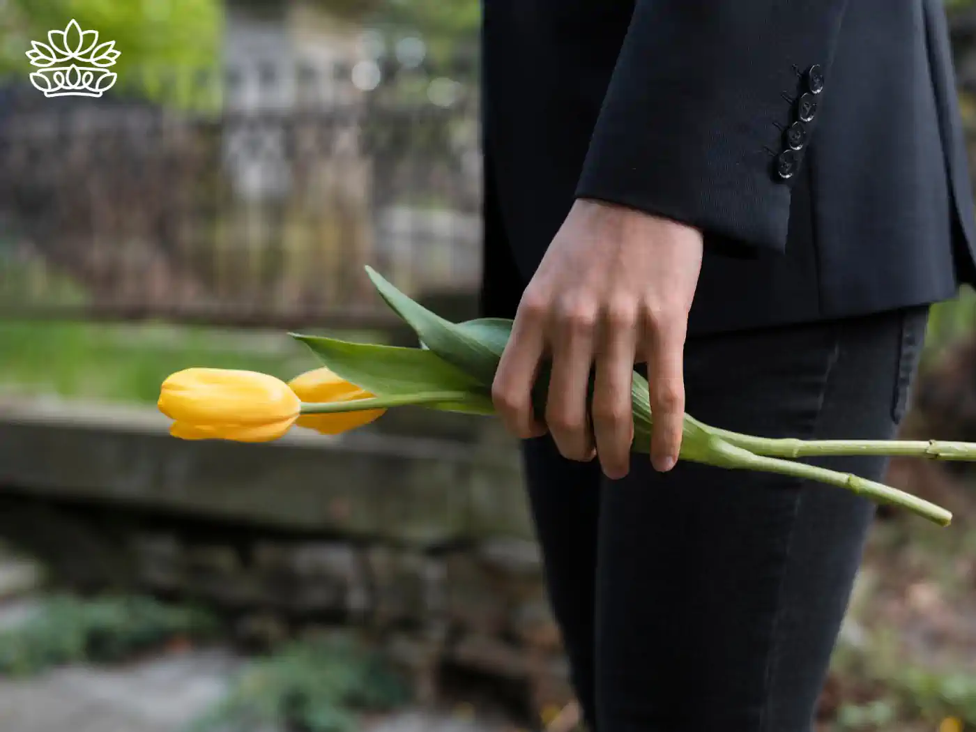 Close-up of a person in a black suit holding a single yellow tulip. Symbolizing remembrance and sympathy at a funeral. Fabulous Flowers and Gifts.