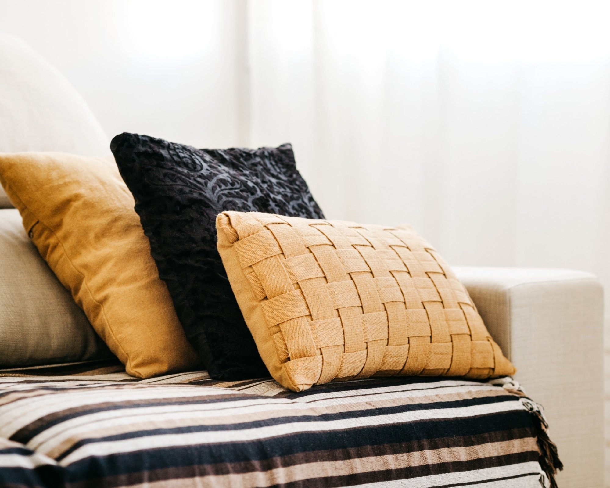 Clean beige sofa with decorative mustard and black pillows, styled with a striped throw blanket in a modern living room, showcasing the results of professional sofa cleaning by Cleanology SG in Singapore.