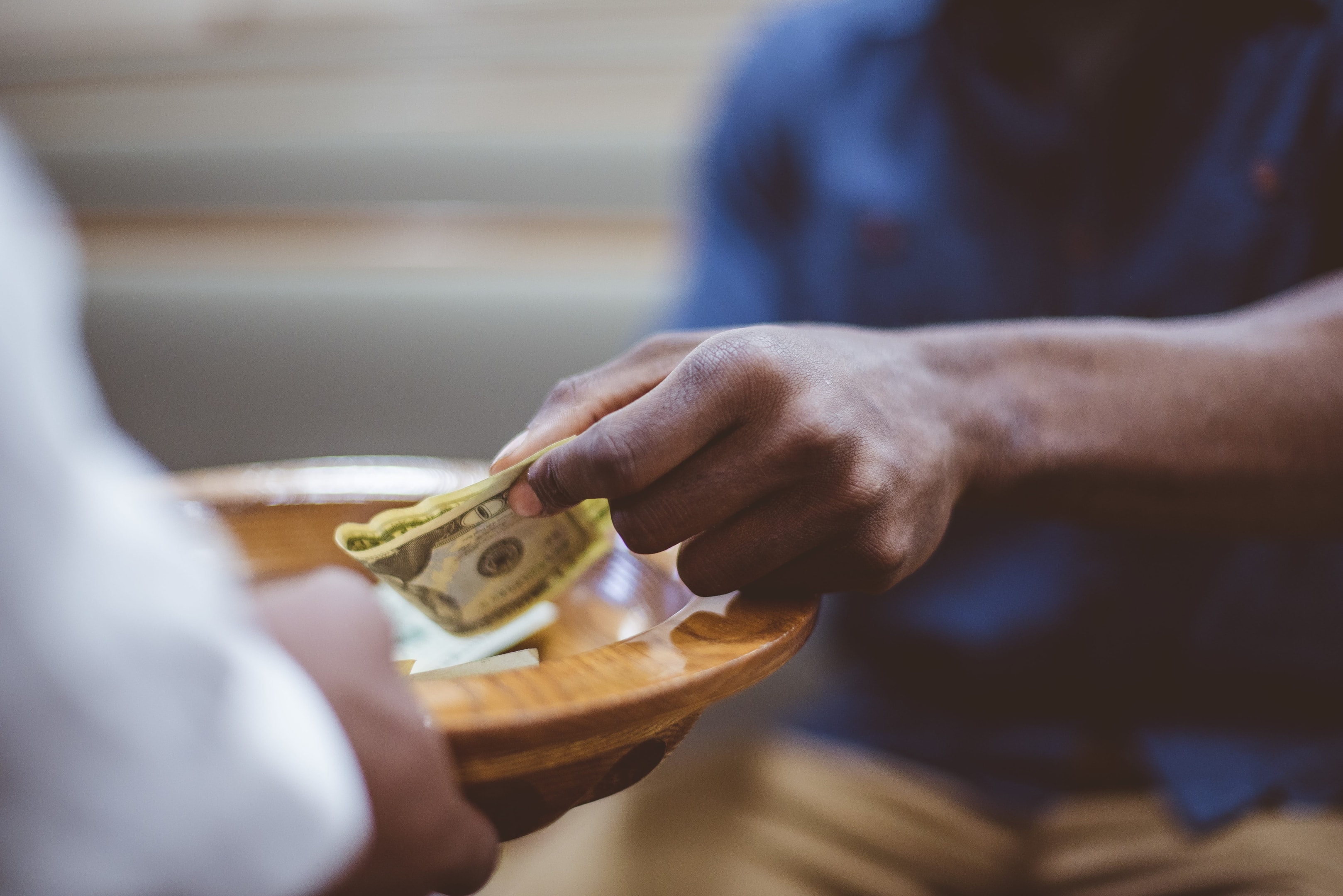 A person placing cash into a church offering plate, representing the importance of including tithing and charitable giving in a faith-based monthly budget.