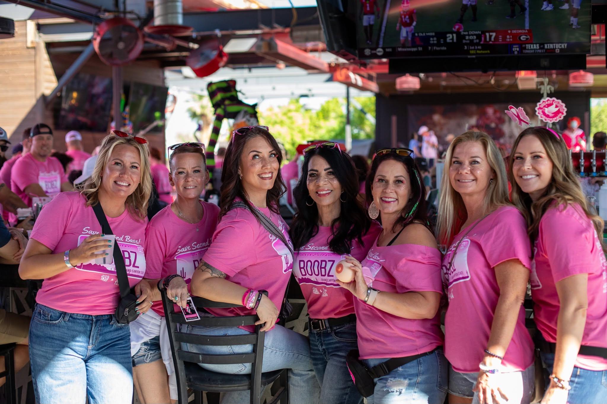 Group of people in pink shirts walking together on a tree-lined path for a breast cancer awareness walk