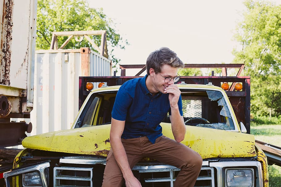 A man standing next to a junk car with a smile on his face