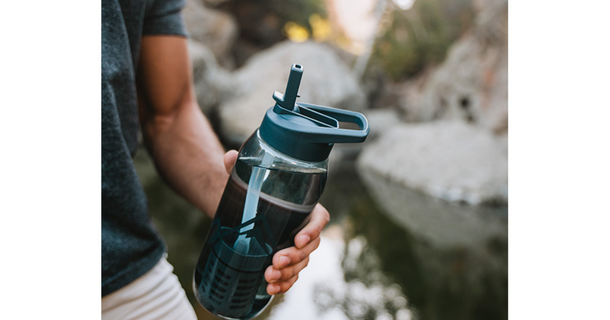 Man holding water bottle in front of a stream - Adventure Wise Travel Gear