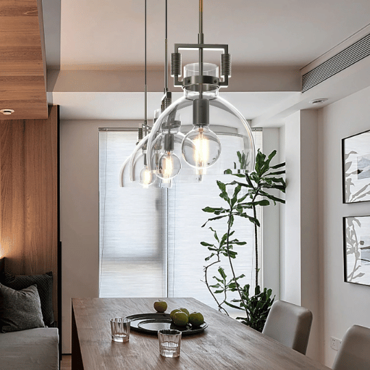 3 industrial-style pendant lights with curved frames illuminating a dining table, featuring a plate with fruit and glasses in a contemporary dining room.