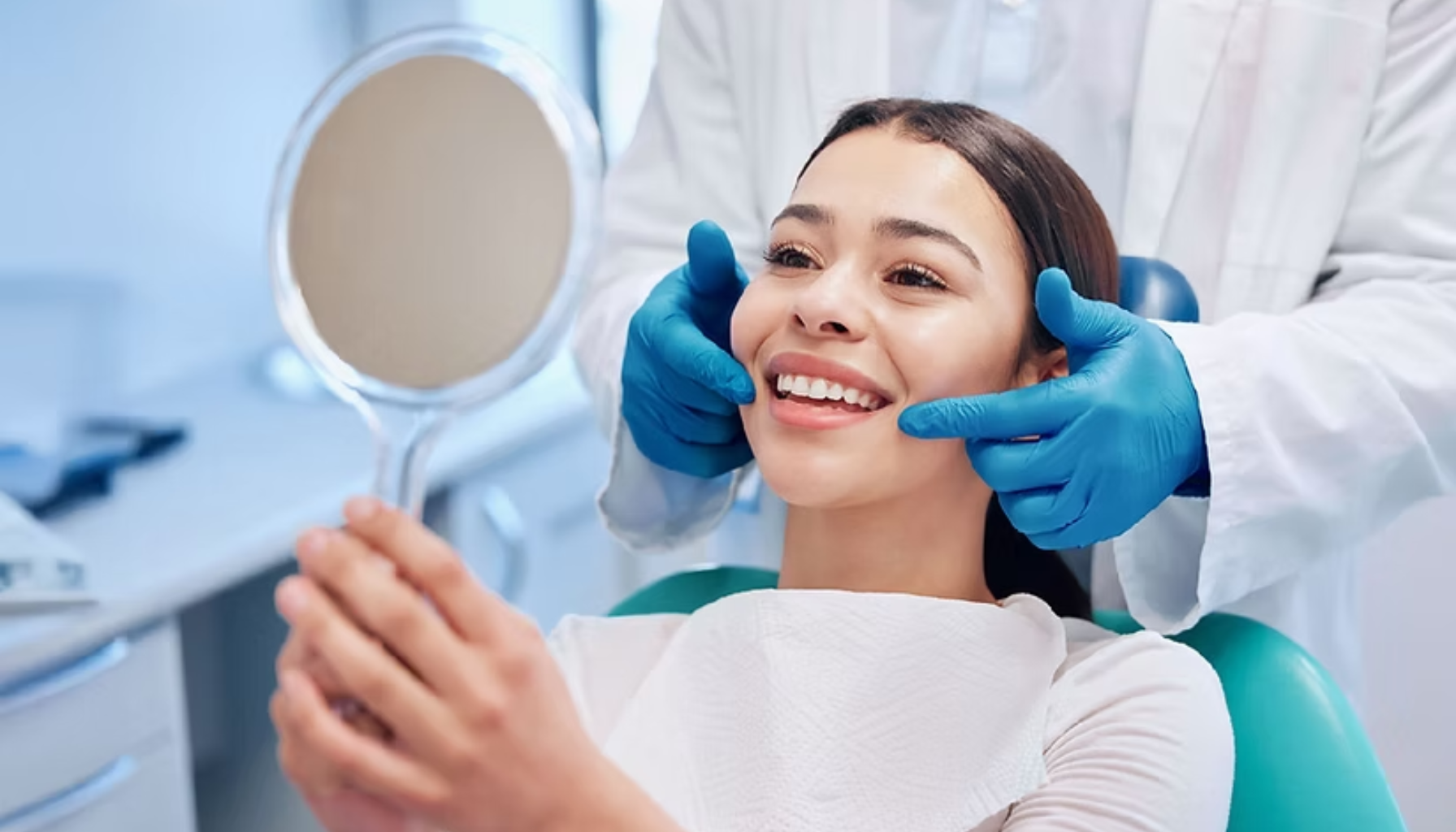 Kvinne sitter i tannlegestol og smiler mens hun ser på resultatet i speil etter behandling.