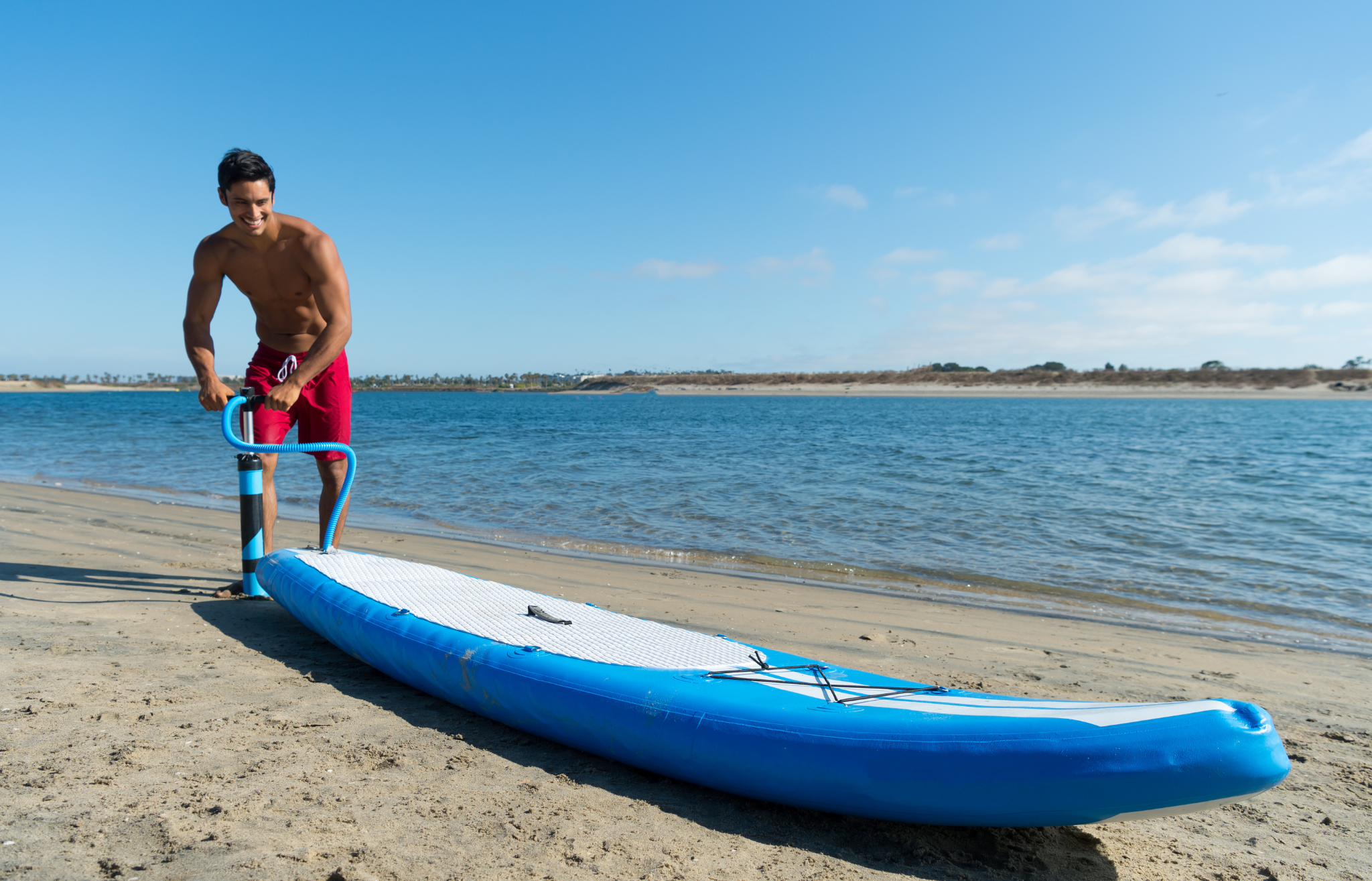 Man on beach inflating stand up paddle board - Adventure Wise Travel Gear