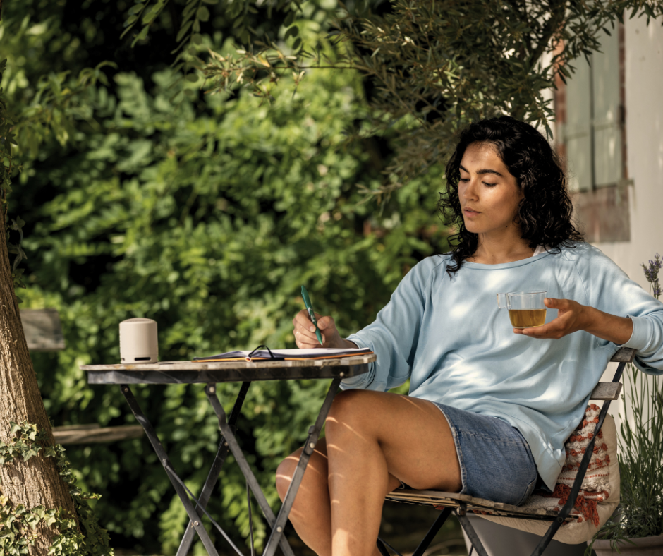 a woman with a cup of tea sits outside journaling