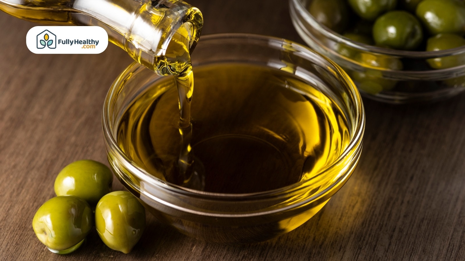 Olive oil pouring into glass bowl with green olives nearby
