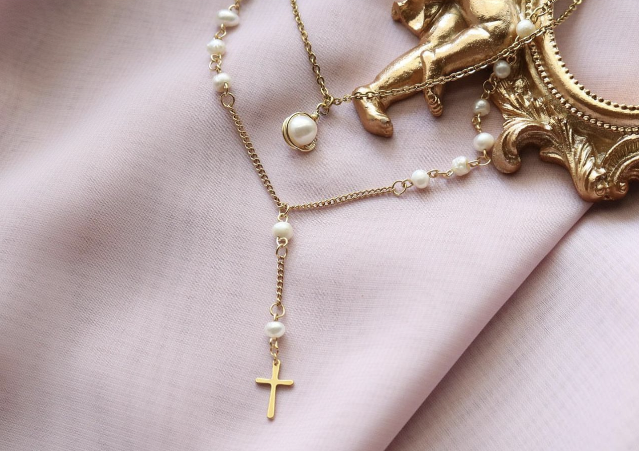 Close-up of a single-pearl necklace and a cross drop pearl necklace on a pink cloth, showcasing the jewelry's delicate design.