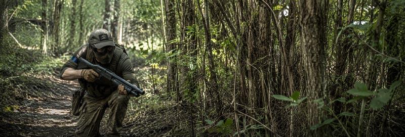 an airsoft player in woodlands with an airsoft shotgun.