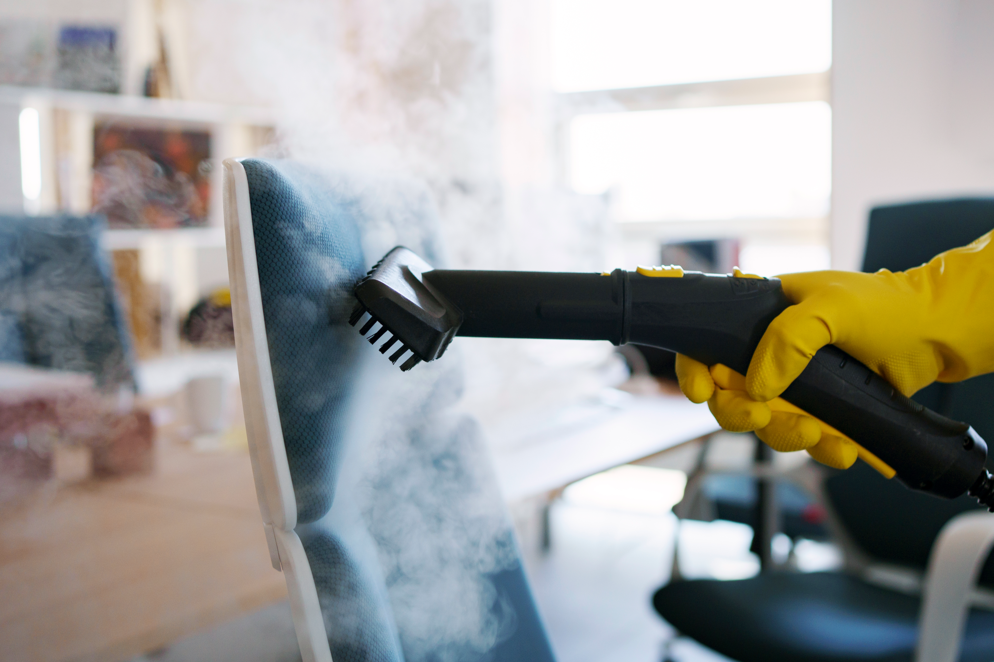 A person using a steam cleaner to clean upholstered furniture