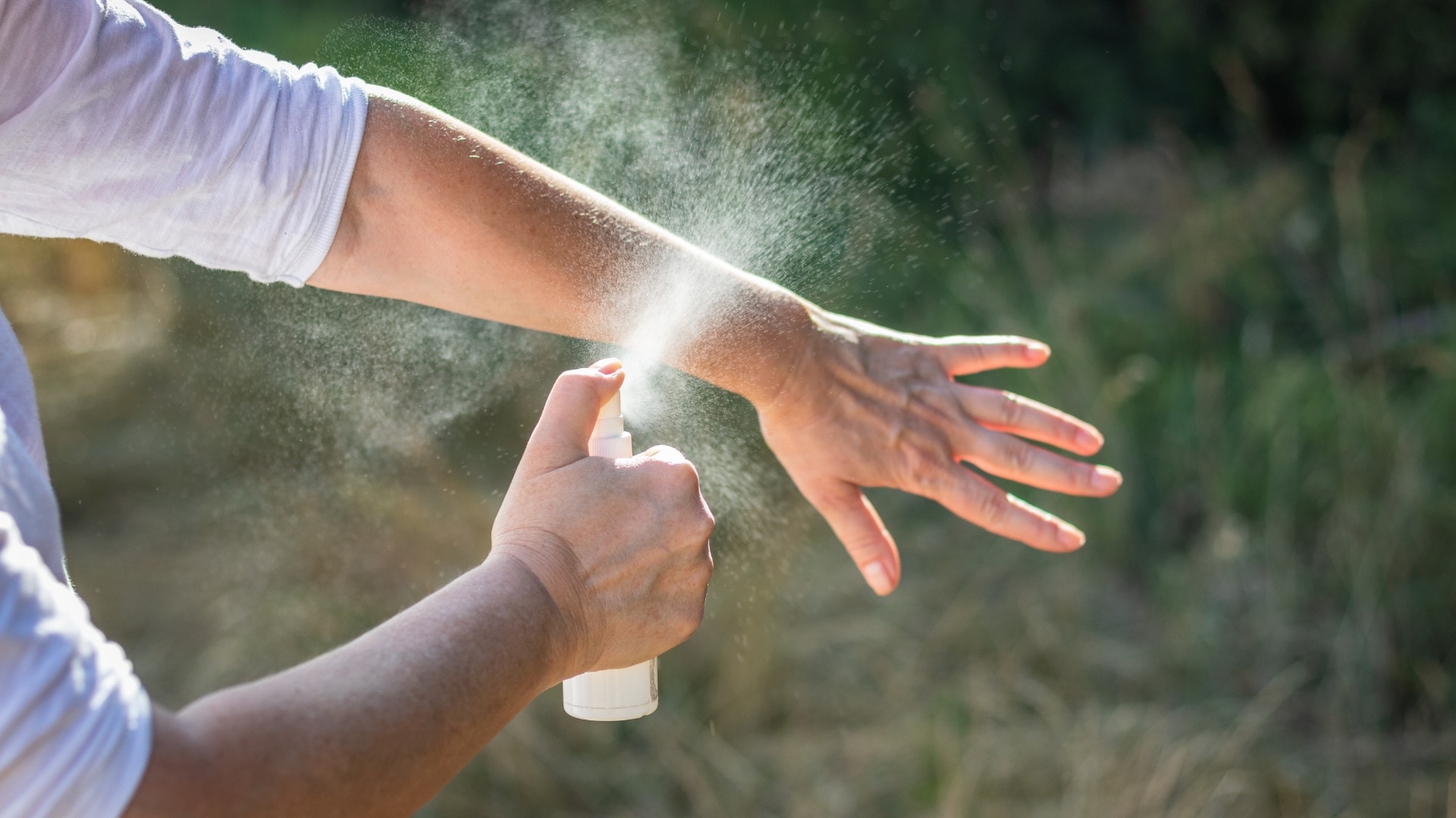 A person spraying mosquito repellent on their arm.