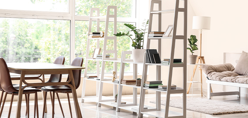A set of four white ladder shelves are being used to separate a dining room and lounge room setting.