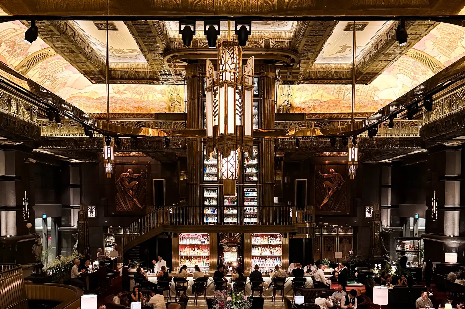 Eye‑level wide‑angle shot of Atlas Bar Singapore showcasing its grand Art Deco interior, towering backlit gin shelves, ornate gold detailing, and guests seated across the main bar and dining area.