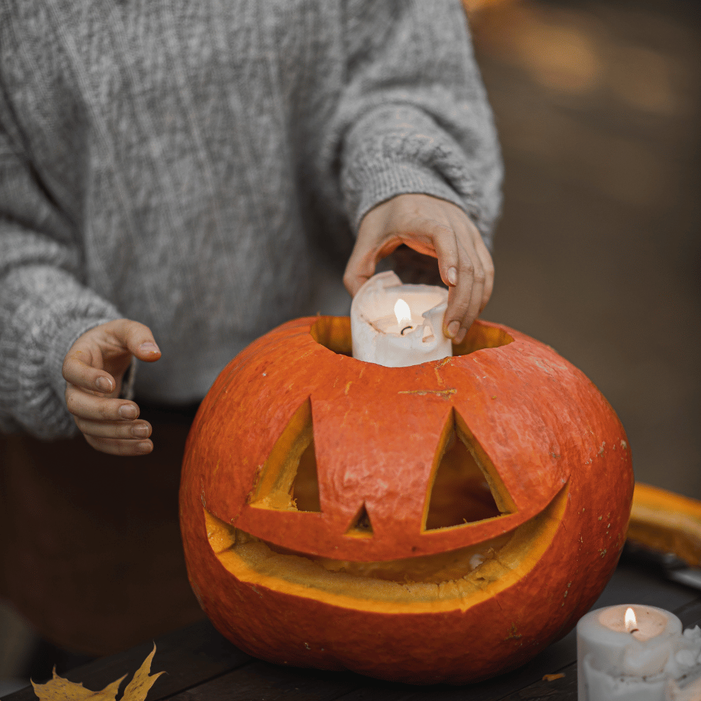 An image of a person inserting a candle into a carved pumpkin