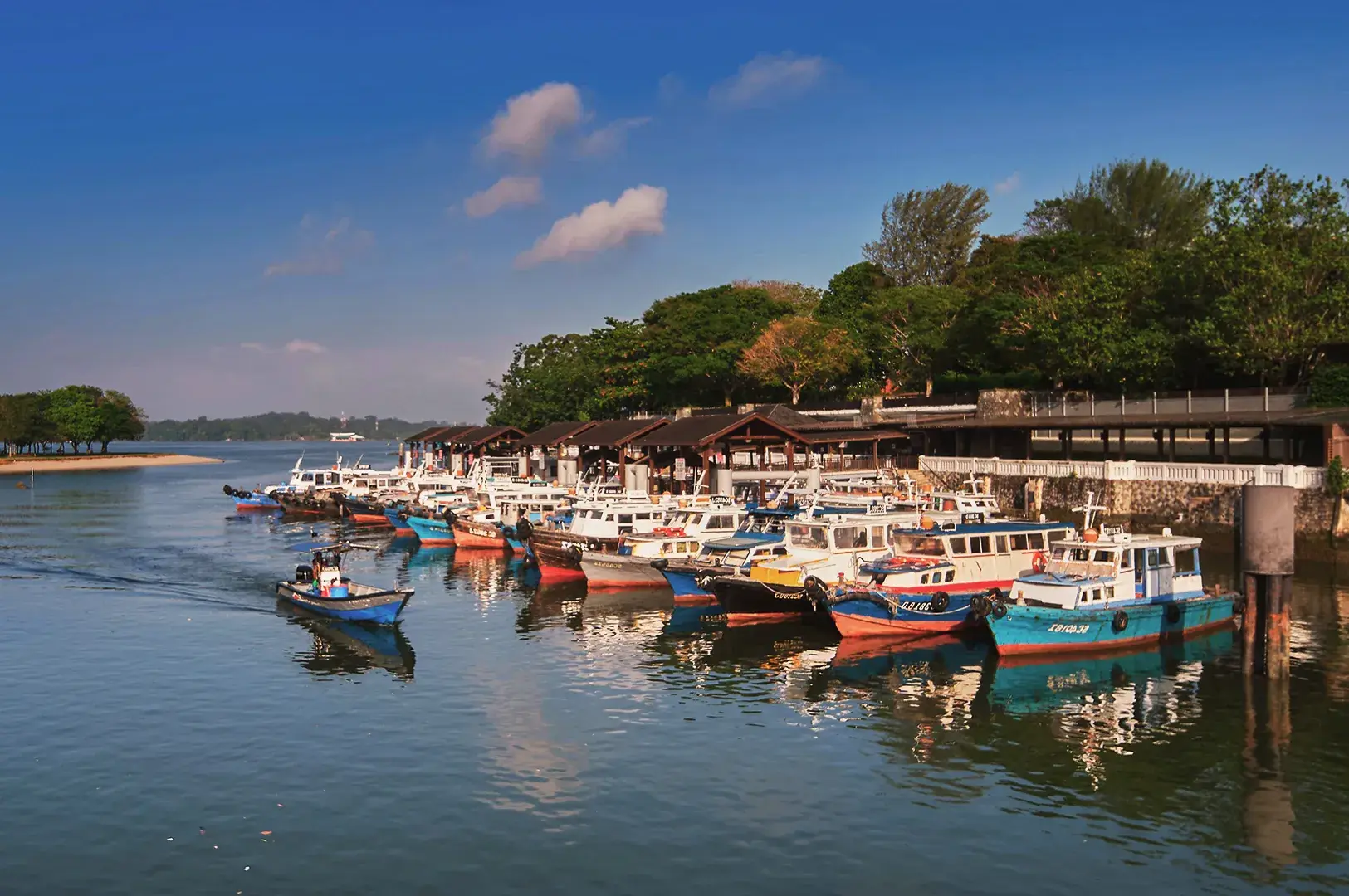 Fishing boats moored at Pulau Ubin jetty under clear blue sky, showcasing Singapore’s rustic island charm