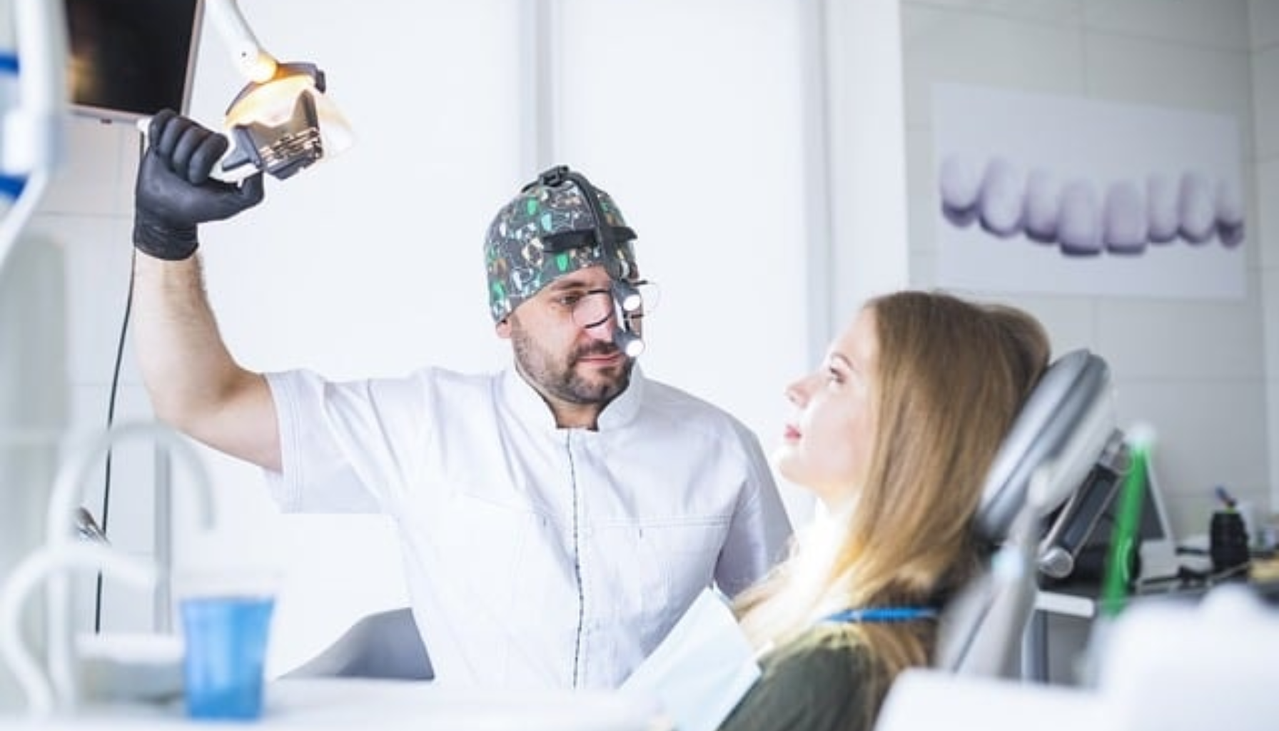 Tannlege med hodelykt og spesialbriller justerer lys over pasient i tannlegestol.