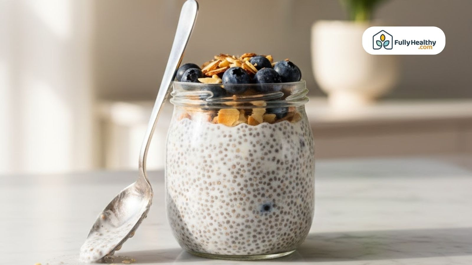 Glass jar of chia pudding topped with blueberries and granola and spoon on the side.
