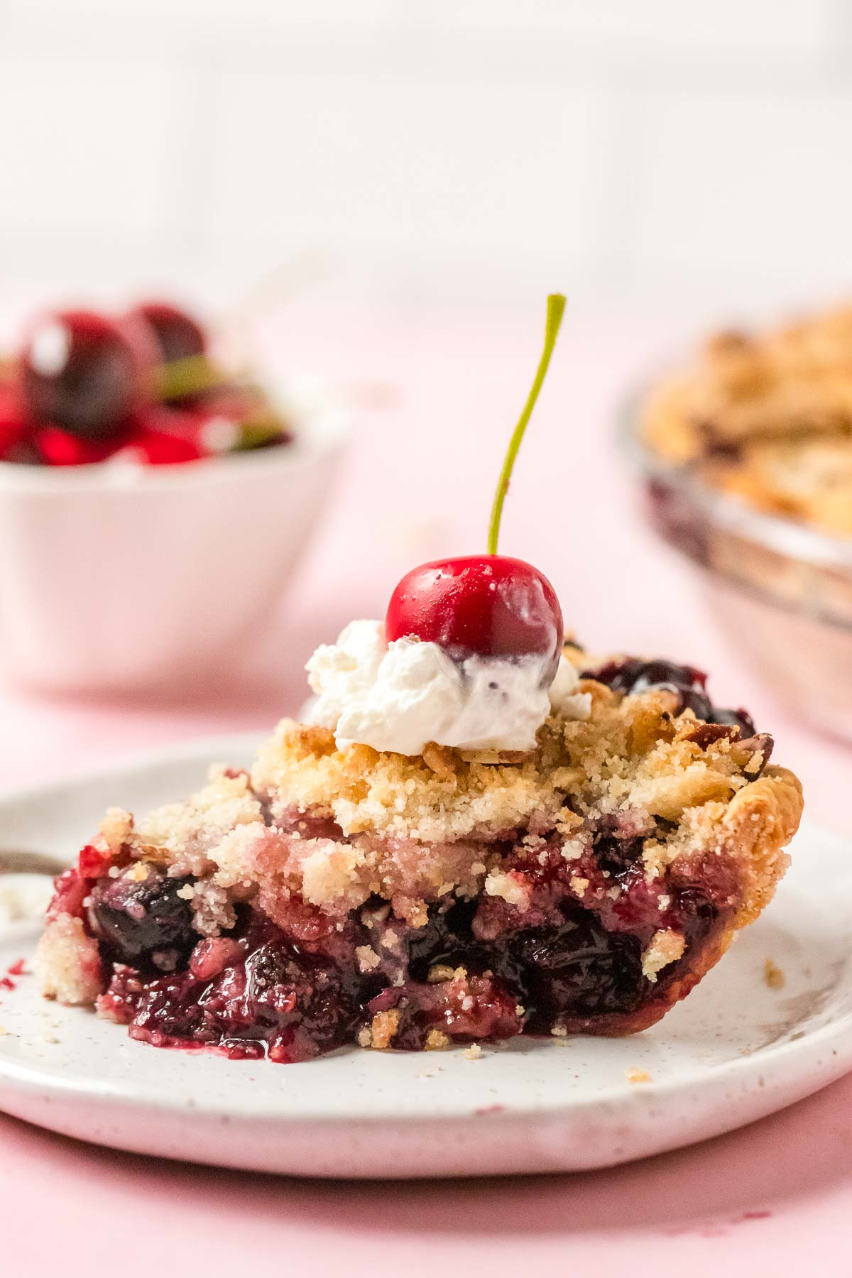 slice of cherry crumb pie on a plate topped with whipped cream and a cherry