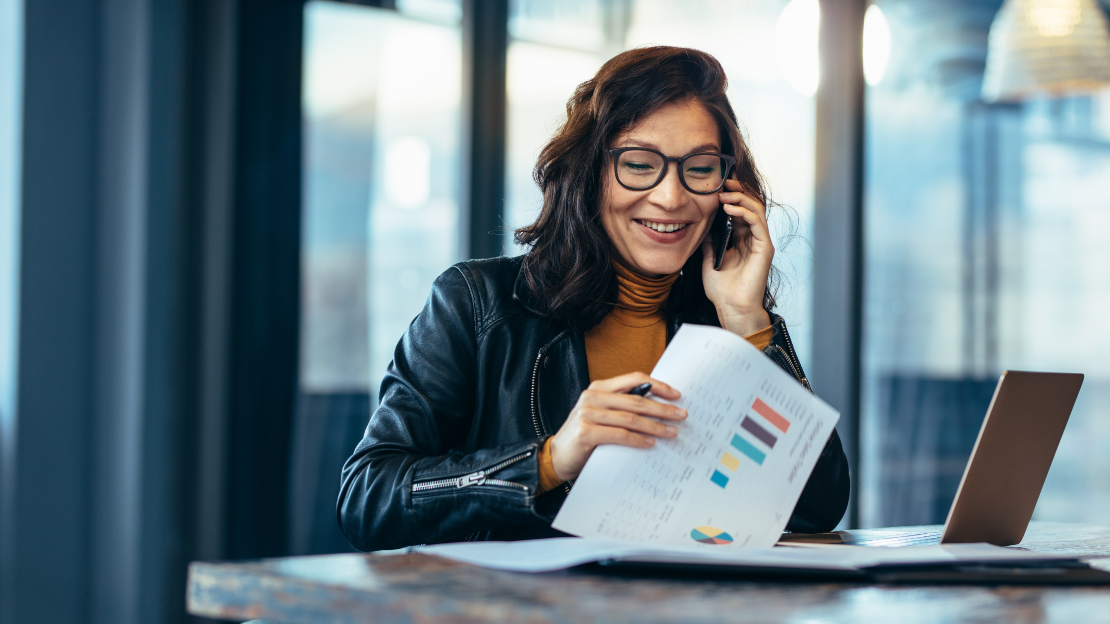 Smiling woman on a phone call reviewing data charts, showing how TEM solutions help enterprise businesses manage expenses, improve customer satisfaction, and monitor revenue trends.