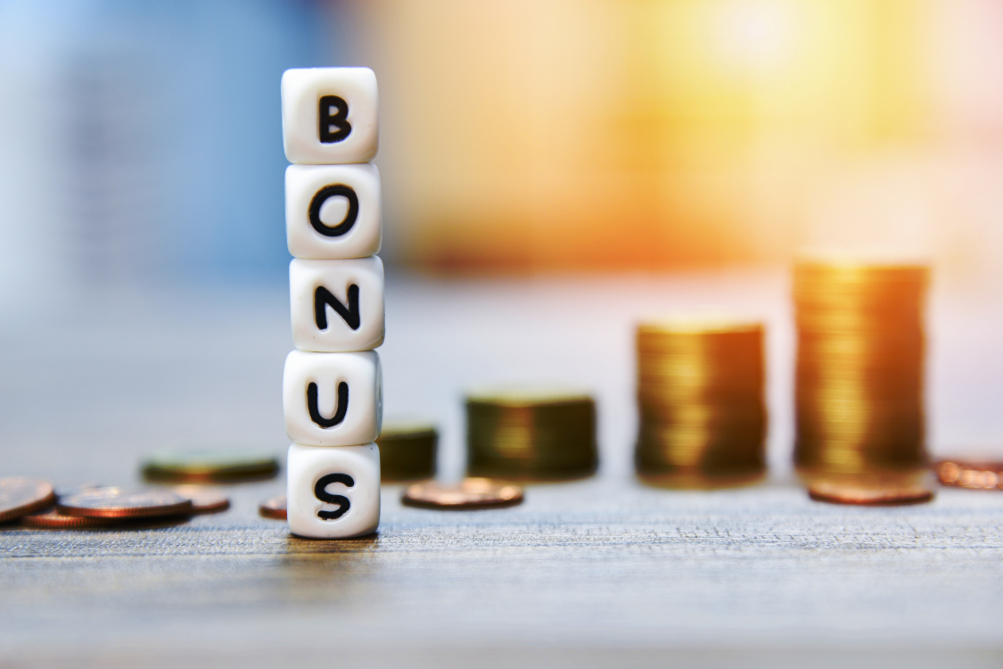 Dice spelling out the word bonus with stacked coins in the background symbolizing performance incentives and compensation benefits