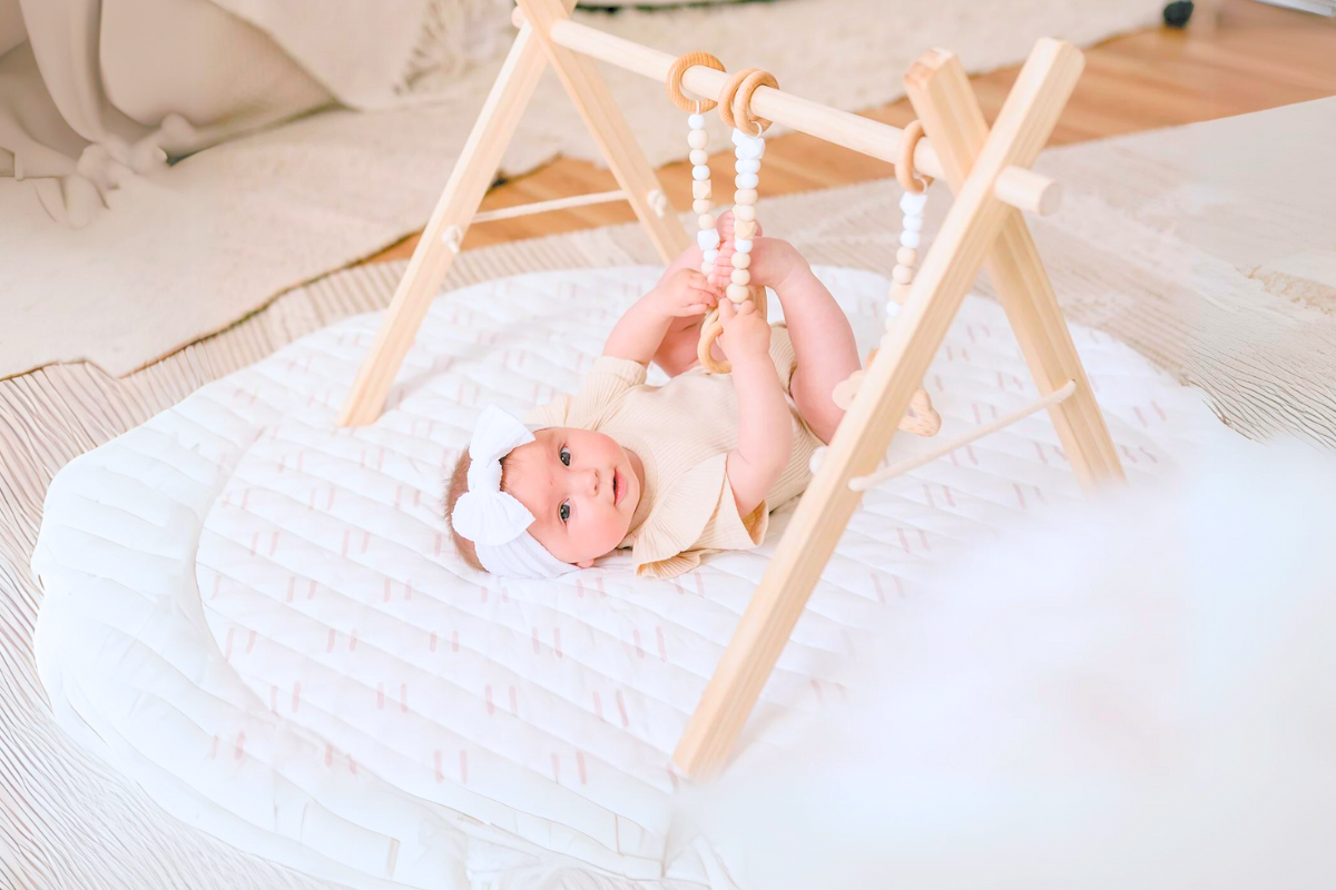 Baby doing floor time under a play gym by poppyseed play