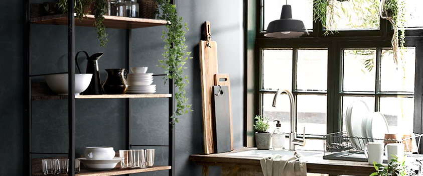 An Artiss Wood and Metal Bookshelf in a dark painted kitchen. It holds a variety of crockery and glasses. A lush vine is draped over the right side.