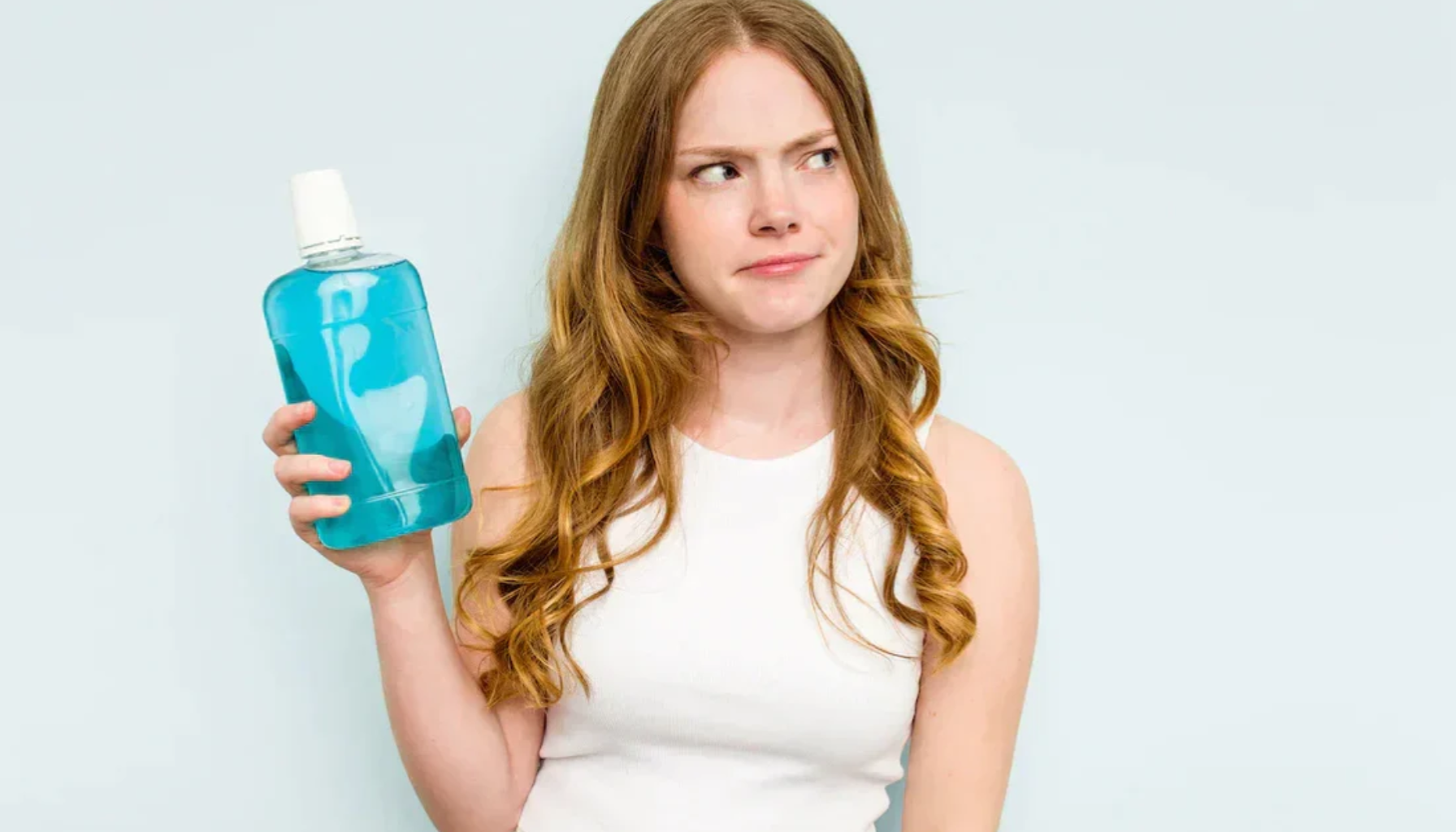 Munnskyll: Når Det Er Nyttig og Når Du Ikke Trenger Det 15 Kvinne holder munnskyllflaske og ser tvilende til siden mot lys bakgrunn.