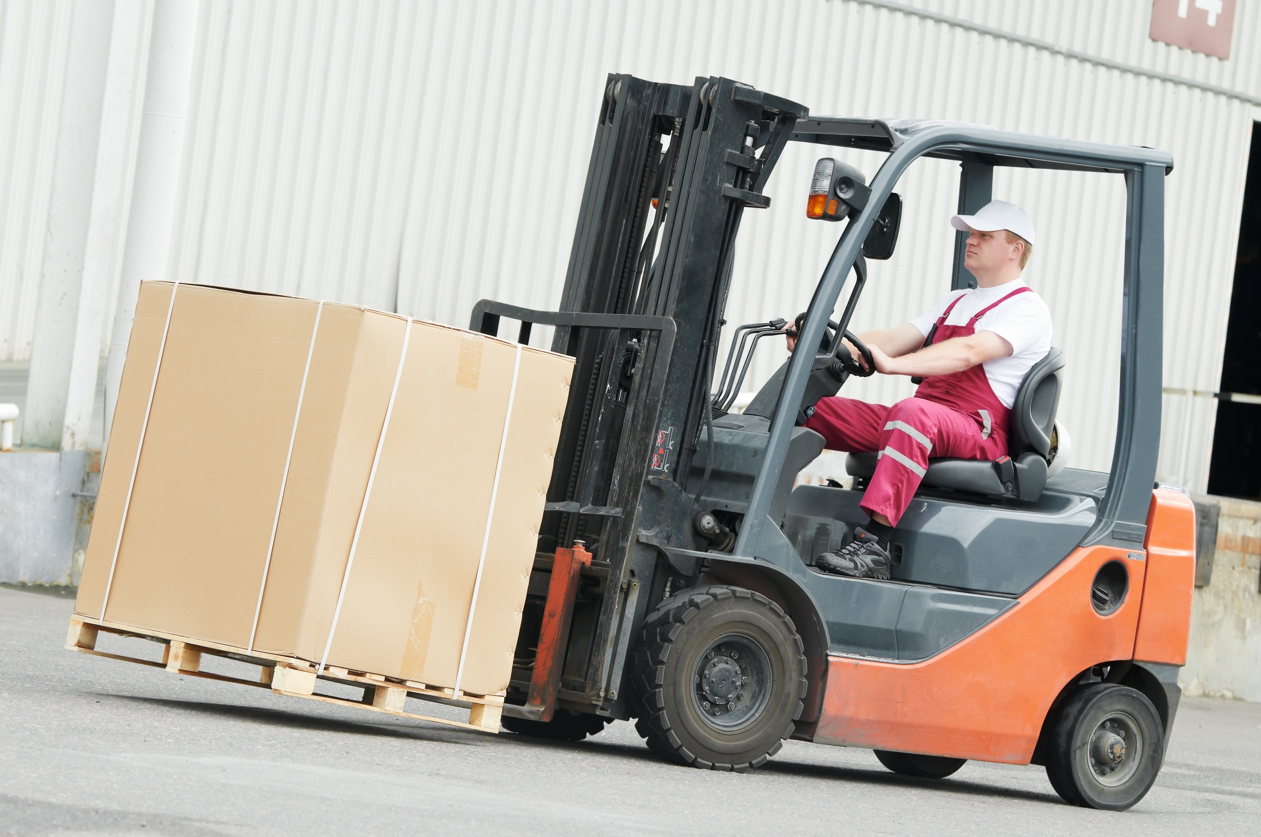 A man in red overalls driving a forklift with a box on the front