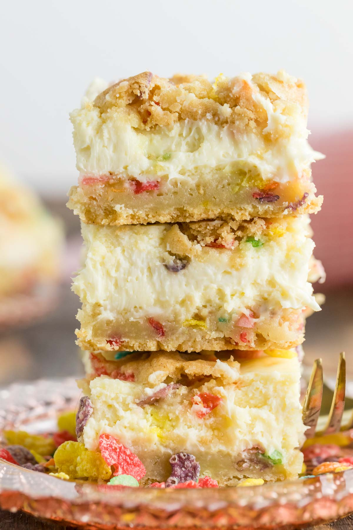 three fruity pebble cheesecake bars stacked on a plate