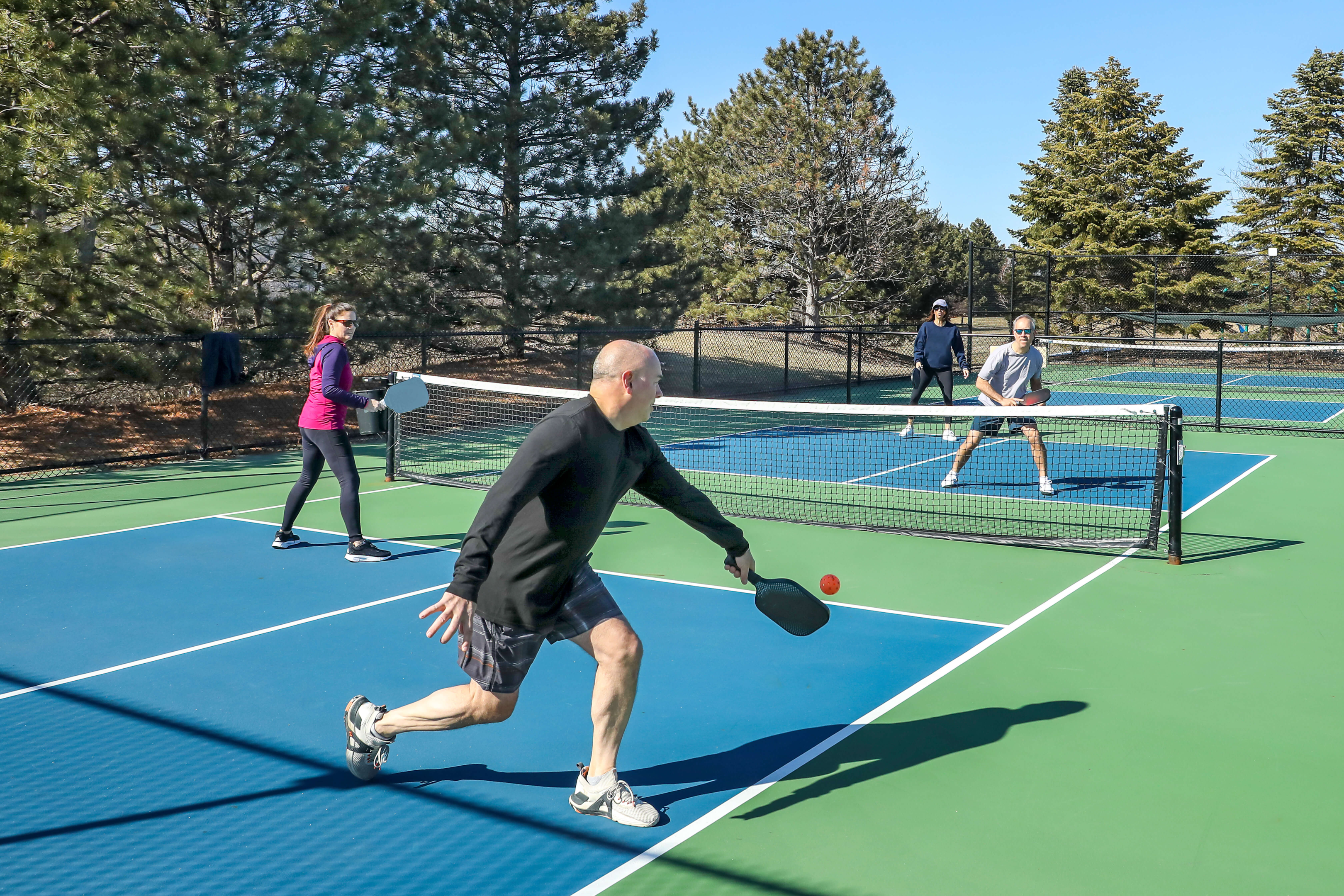 Pickleball game of two teams: The male player in black shirt is trying to hit the ball in his side of the court.